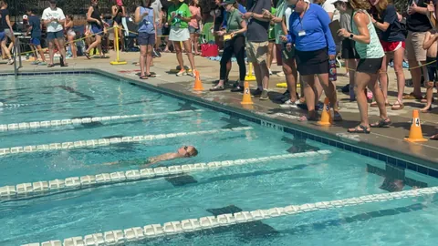 A young swimmer races down a lane as timekeepers watch from poolside.