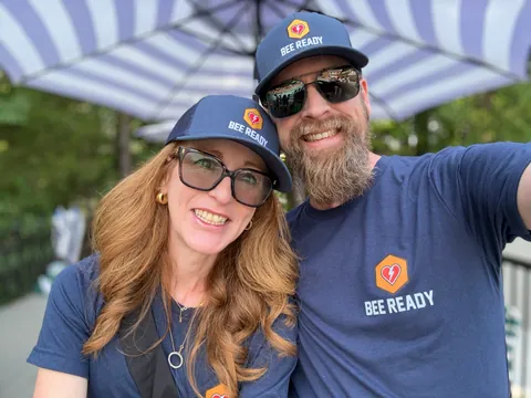 Two Bee Ready volunteers in branded hats and shirts at the swim meet booth.